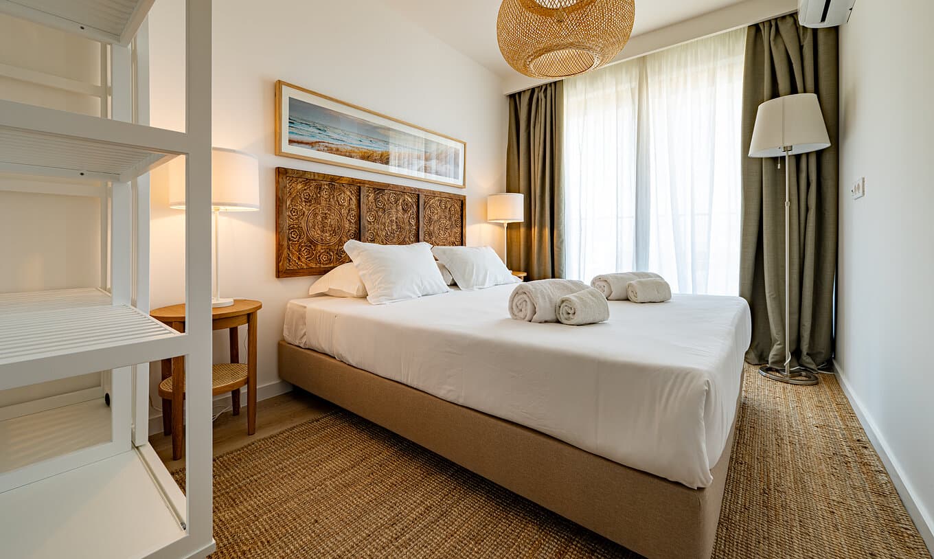 Calm bedroom with white linens, a carved wood headboard and olive curtains