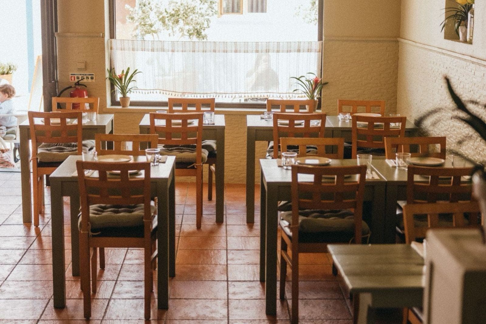 The dining room at Figo, wooden tables on a tiled floor beneath tall street-facing windows