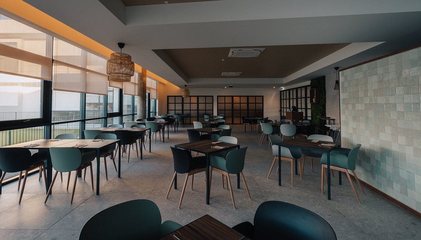 The dining room at Slow Sea, teal chairs and a green tiled wall under long windows