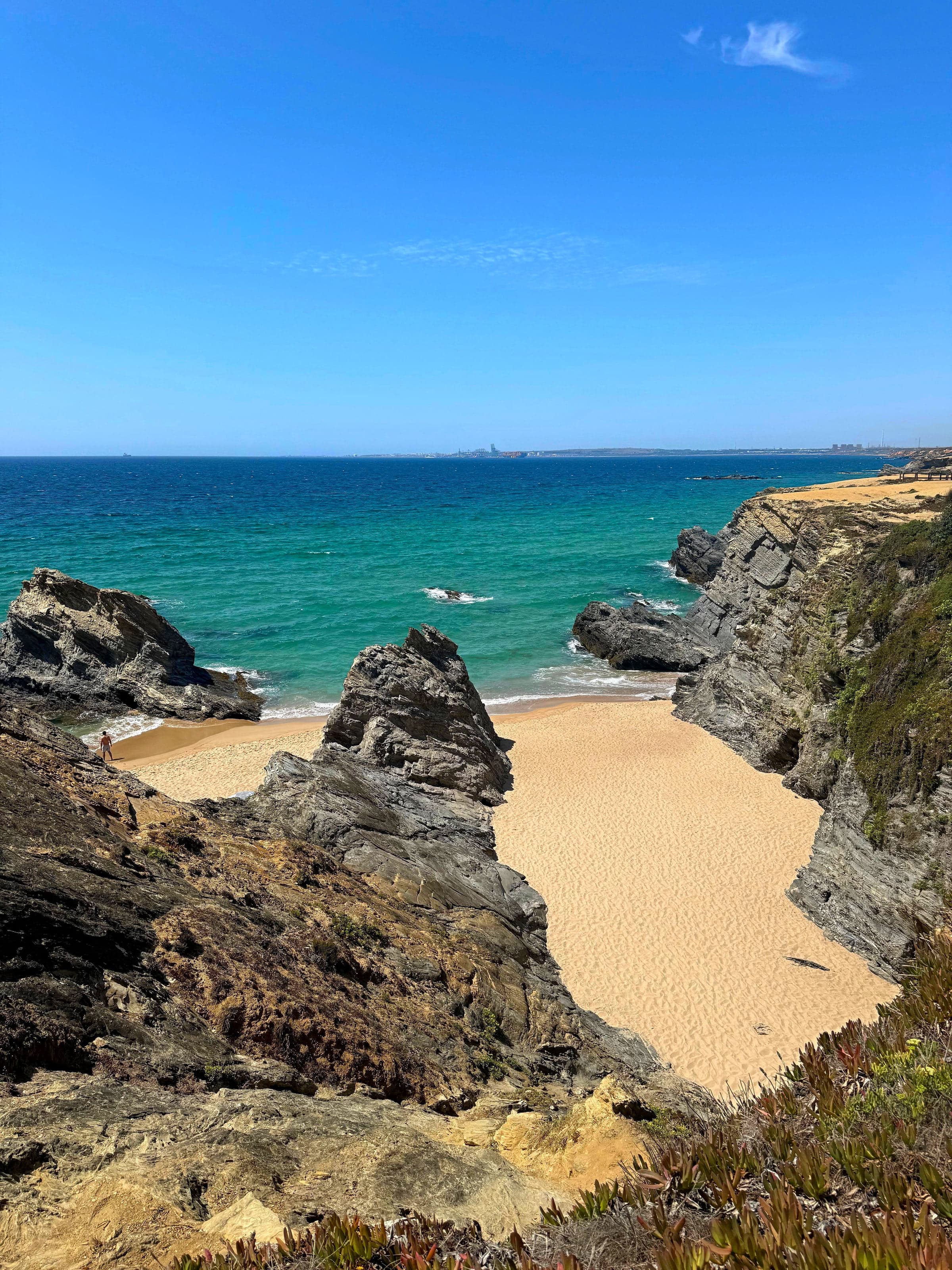 A rock stack standing on the empty golden sand of a Porto Covo beach cove